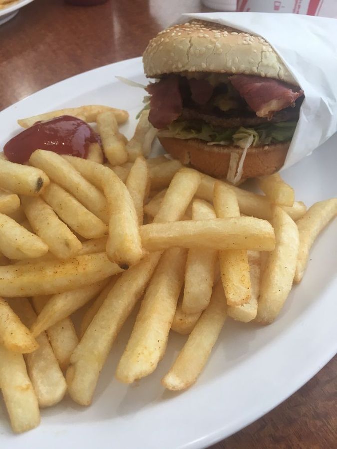 Bacon burger wrapped in paper with a pile of golden fries