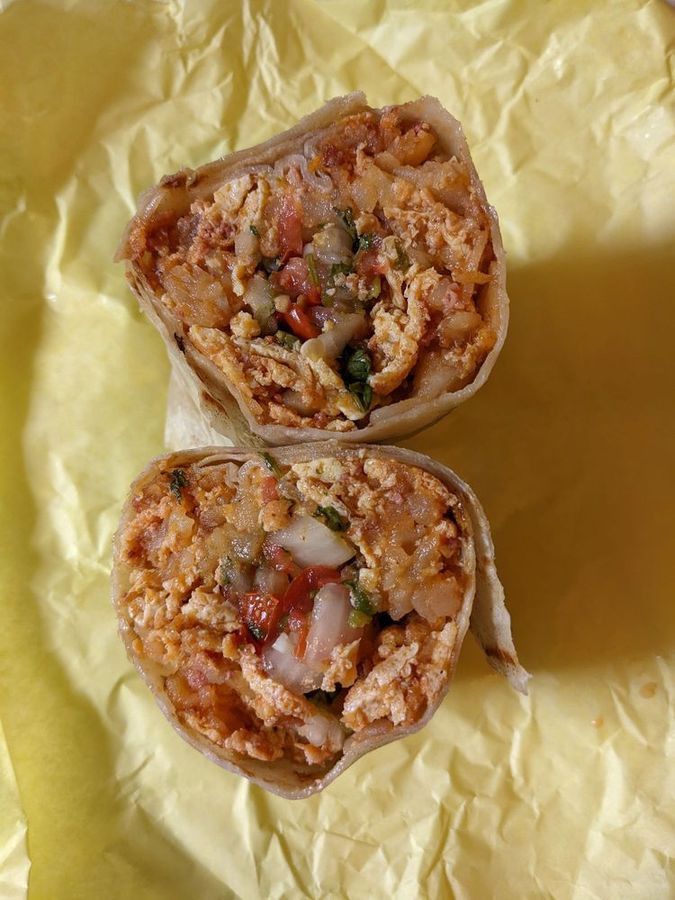 Pete's breakfast burrito cut in half on yellow burger paper, packed with scrambled eggs, potatoes, bacon and pico de gallo
