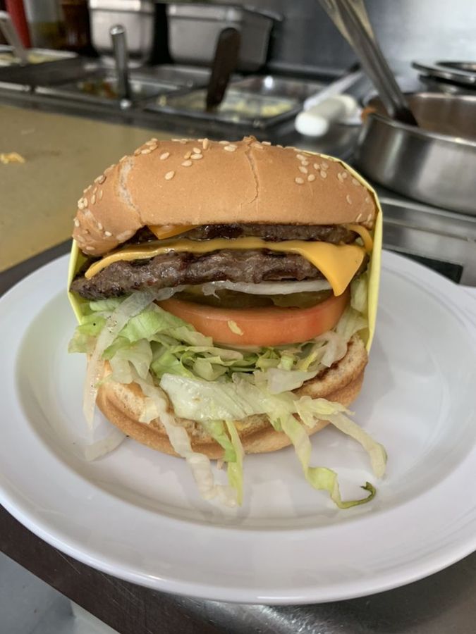 Double cheeseburger in Pete's yellow wrap paper — melted cheese, tomato, pickles and shredded lettuce on a sesame bun