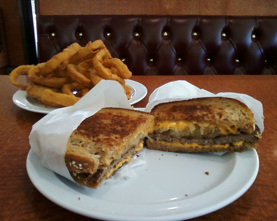 Patty melt cut in half with a side of onion rings on a booth table at Pete's